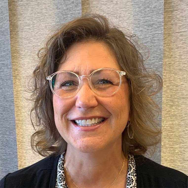 A portrait photo of a smiling woman with curly hair and large glasses